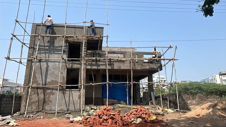 Workers plastering a small house on bamboo scaffolding